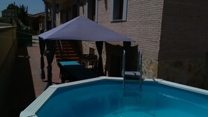 A swimming pool with a ladder, a covered seating area, and a stone building in the background.