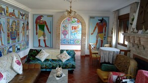 A room with Egyptian-themed wall art, a sofa, a small table, and a fireplace.