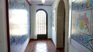 A hallway with tiled floors, a door with a decorative arch, and walls adorned with colorful patterns.