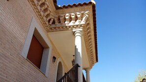 Un edificio con fachada de ladrillo, puerta roja y balcón con barandilla blanca ornamentada.