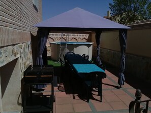 Un patio con mesa y sillas bajo una pérgola, una piscina pequeña y una parrilla.