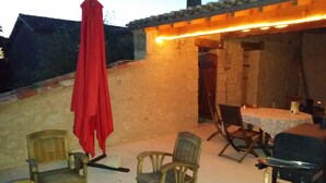 Una veranda esterna con mobili in vimini, un tavolo con tovaglia bianca e un ombrello rosso.