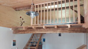 Una scala in legno conduce a una zona mansardata con ringhiera in metallo e lampadario.