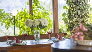 Mesa de comedor lista con platos, vasos y flores, con vista a la vegetación.