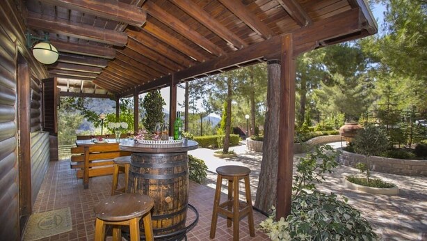 Un patio al aire libre con mobiliario de madera, un barril grande y vistas a un jardín ajardinado.