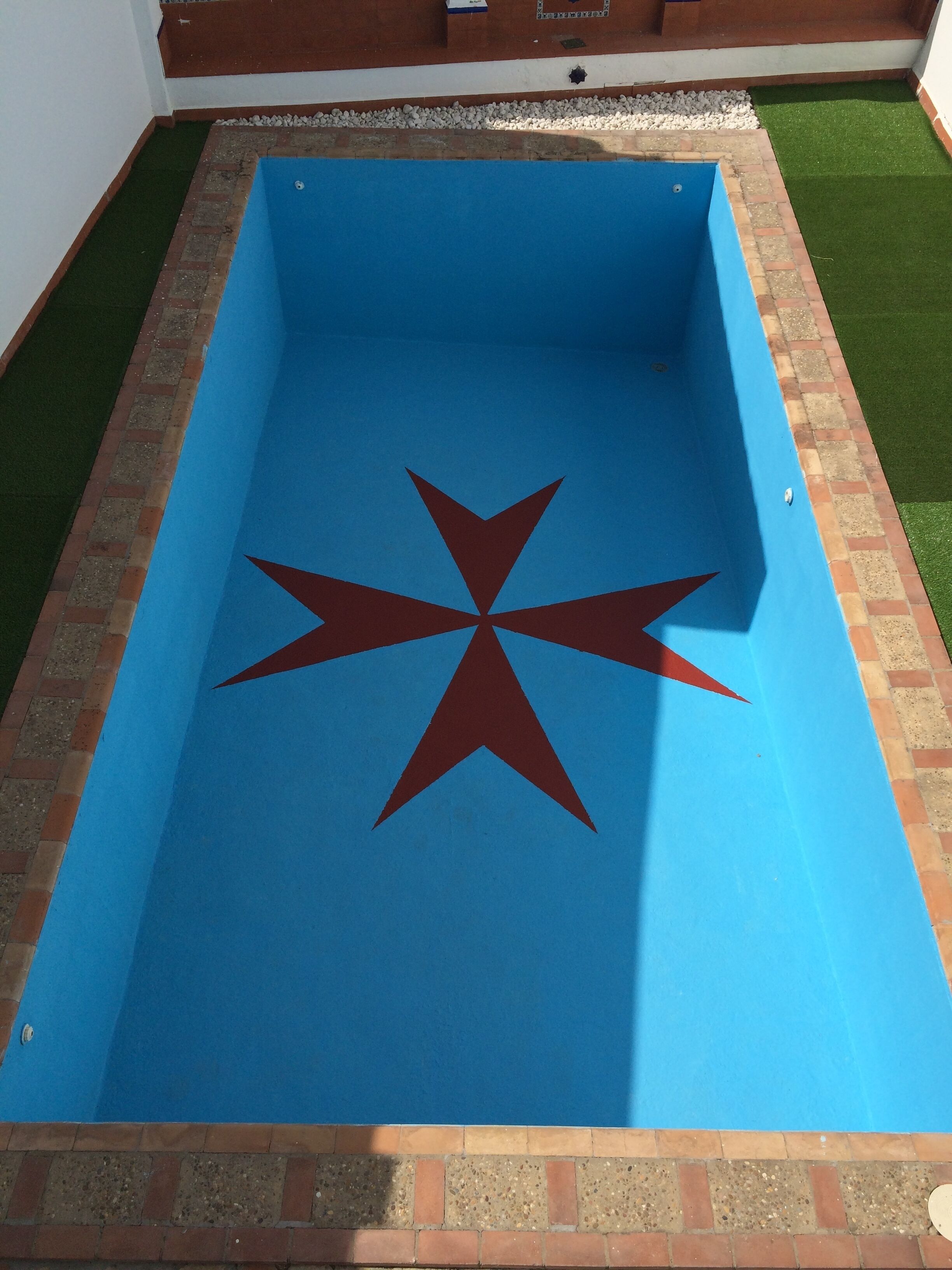 Une piscine rectangulaire dont l’intérieur est bleu et qui présente un motif en forme d’étoile rouge au centre.