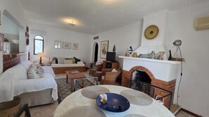 A living room with a fireplace, a sofa, a coffee table, and a dining table. - Apartment 5 minutes from the beach,pool, AC, free parking,400m from the airfield (Alvor)