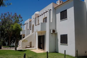 A modern building with a white facade, a covered entrance, and a small garden area with trees and grass.