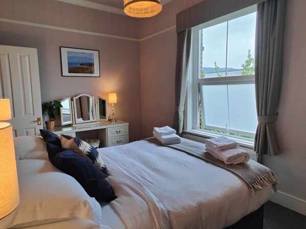 A bedroom with a bed, bedside lamps, a dresser, a mirror, a window with curtains, and a framed picture on the wall.