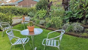 Um pequeno jardim bem cuidado com uma mesa redonda e quatro cadeiras de metal.