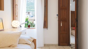 A bedroom with a bed, a window with curtains, a wooden door, and a view of buildings and greenery outside. - Mlle. BIBI Casa Tipica Soller in center of Soller. Parking at 500m included.  (Sóller)