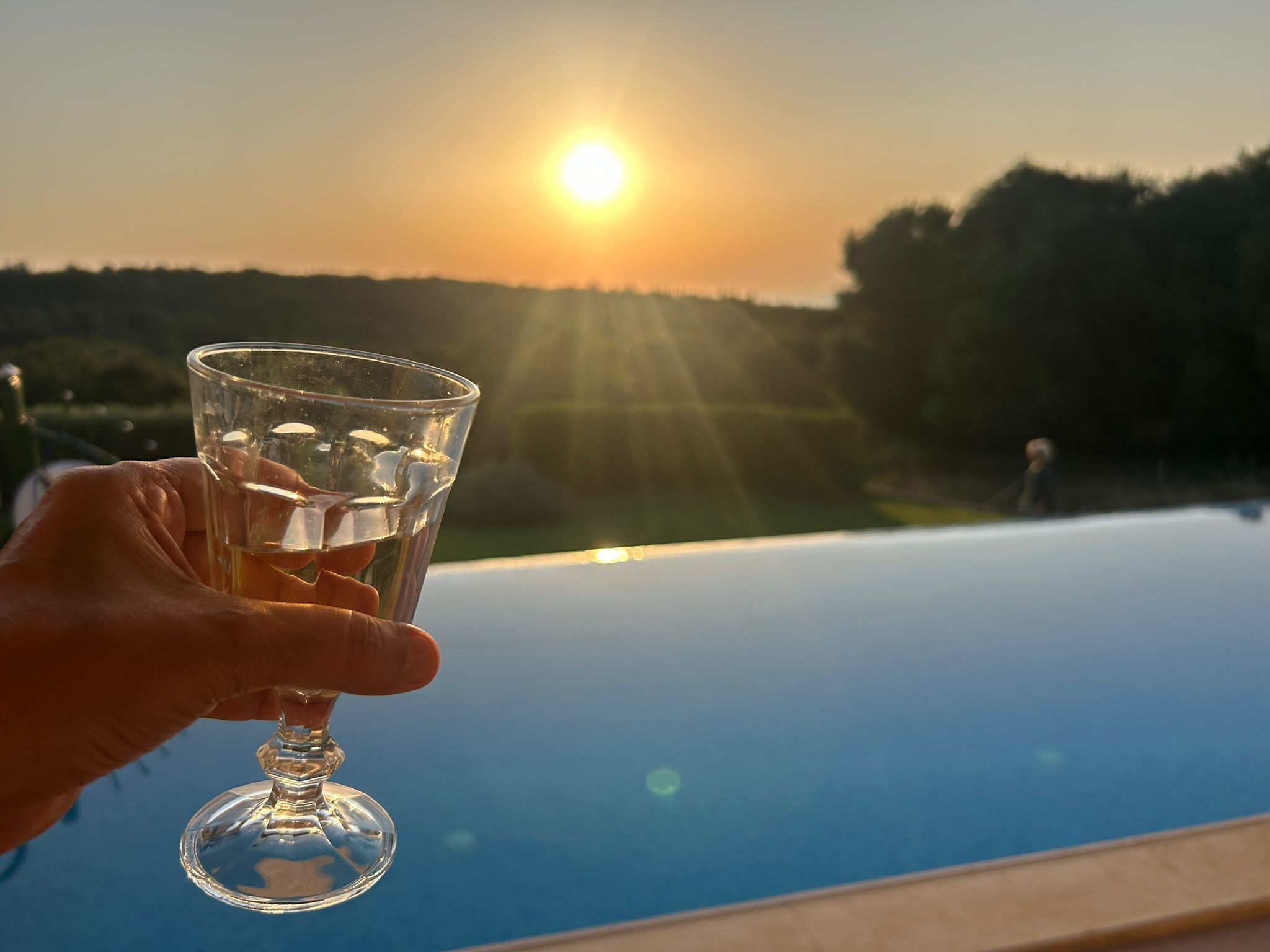 Een hand vasthoudt een glas water, met een zonsondergang op de achtergrond.