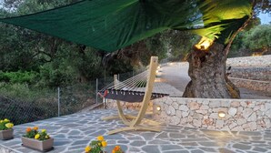 Un hamac suspendu sous une voûte de verdure, entouré de murs de pierre et de pots de soucis.