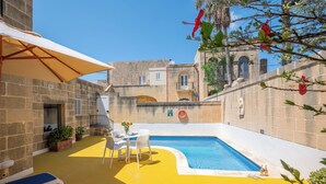 A pool area with a yellow floor, white lounge chairs, and a table with chairs. - Holiday home in Gozo with private pool, quiet location & family friendly  (Gharb)