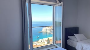 Une chambre d’hôtel dotée d’une grande fenêtre donnant sur une ville côtière et la mer.