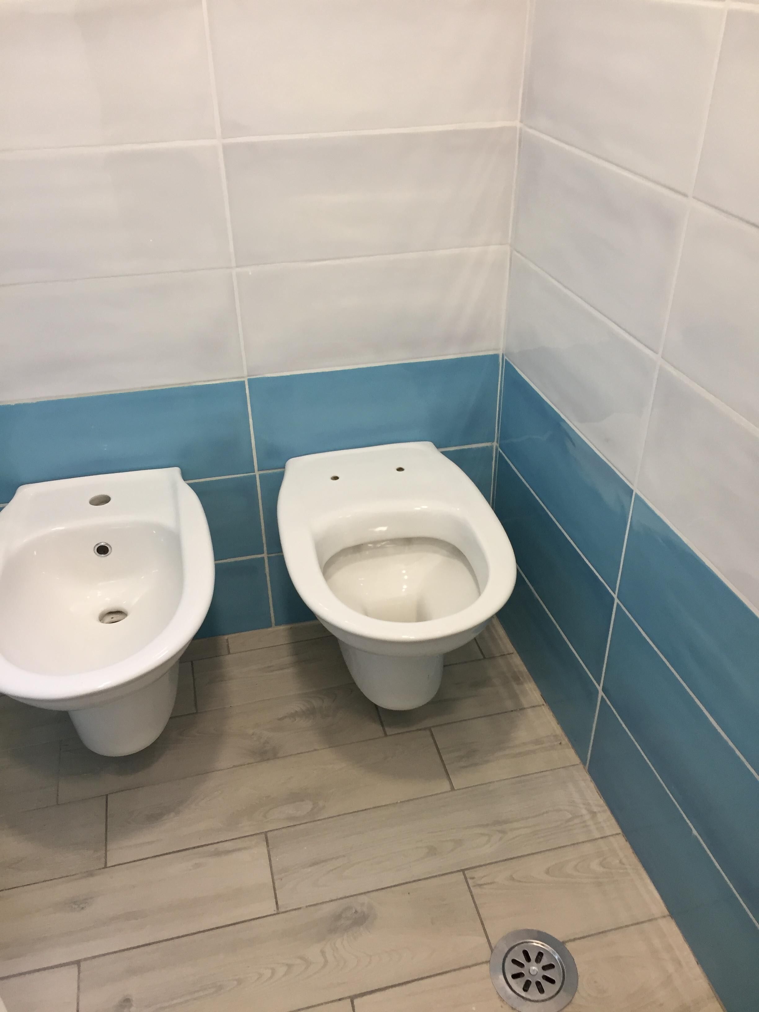 A small bathroom with two toilets and a floor drain.