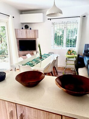 A modern kitchen with a dining table, two large bowls, a TV, and a window with a view of greenery.