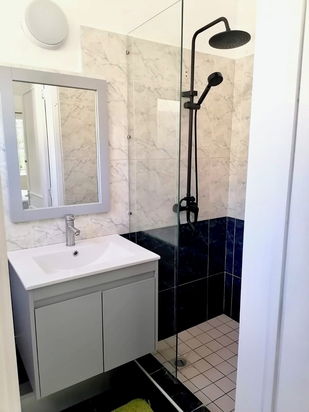 A modern bathroom with a white sink, a mirror, a handheld showerhead, and black and white tiled walls.
