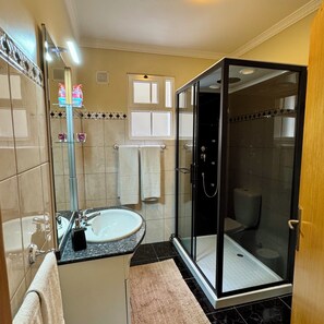 Une salle de bain avec une douche à parois de verre, un lavabo avec un miroir et des toilettes.