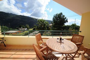 Un balcon avec une table et des chaises en bois, une bouteille de vin et un verre de vin.