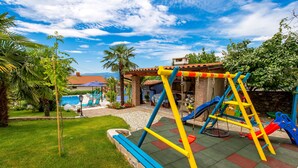 Un parque infantil con columpios y toboganes, rodeado de césped y palmeras.