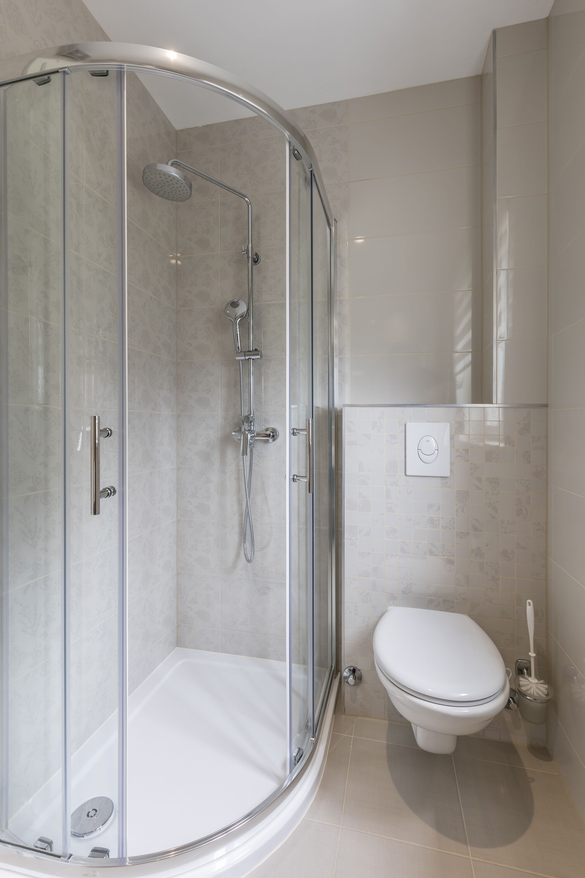 A modern bathroom with a glass-enclosed shower, a white toilet, and a wall-mounted flush handle.