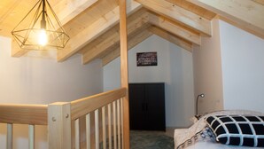 Quarto com teto de madeira, cama com roupa de cama estampada, luminária pendente e uma porta ao fundo.
