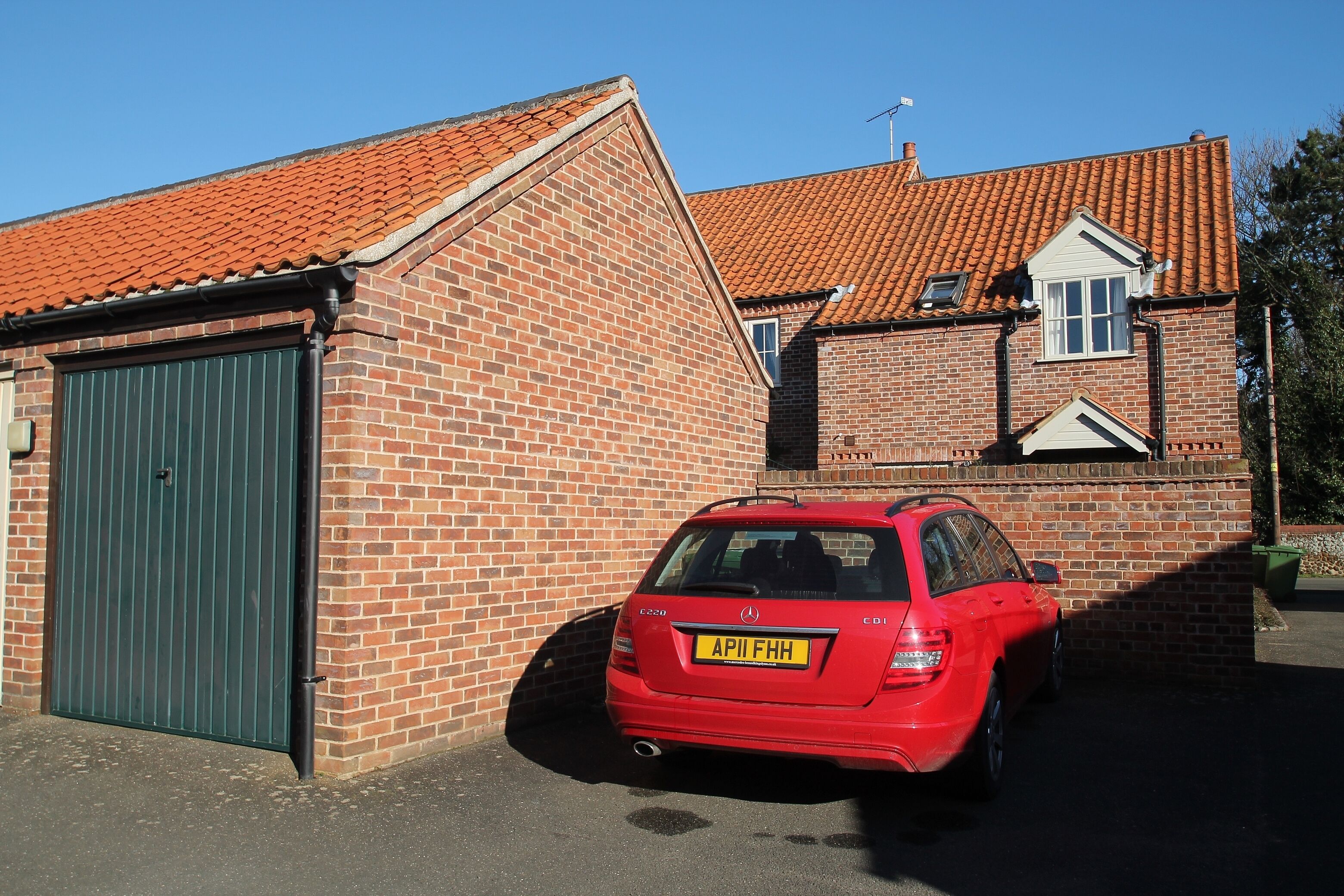 A red car parked in front of a brick building with a green garage door.