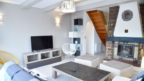 Una sala de estar moderna con un televisor de pantalla plana, muebles blancos, una chimenea de piedra y una escalera de madera.