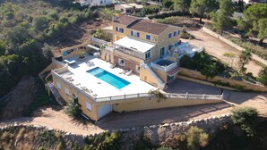 Una casa de dos pisos con piscina, un patio cubierto y un muro de contención de piedra.