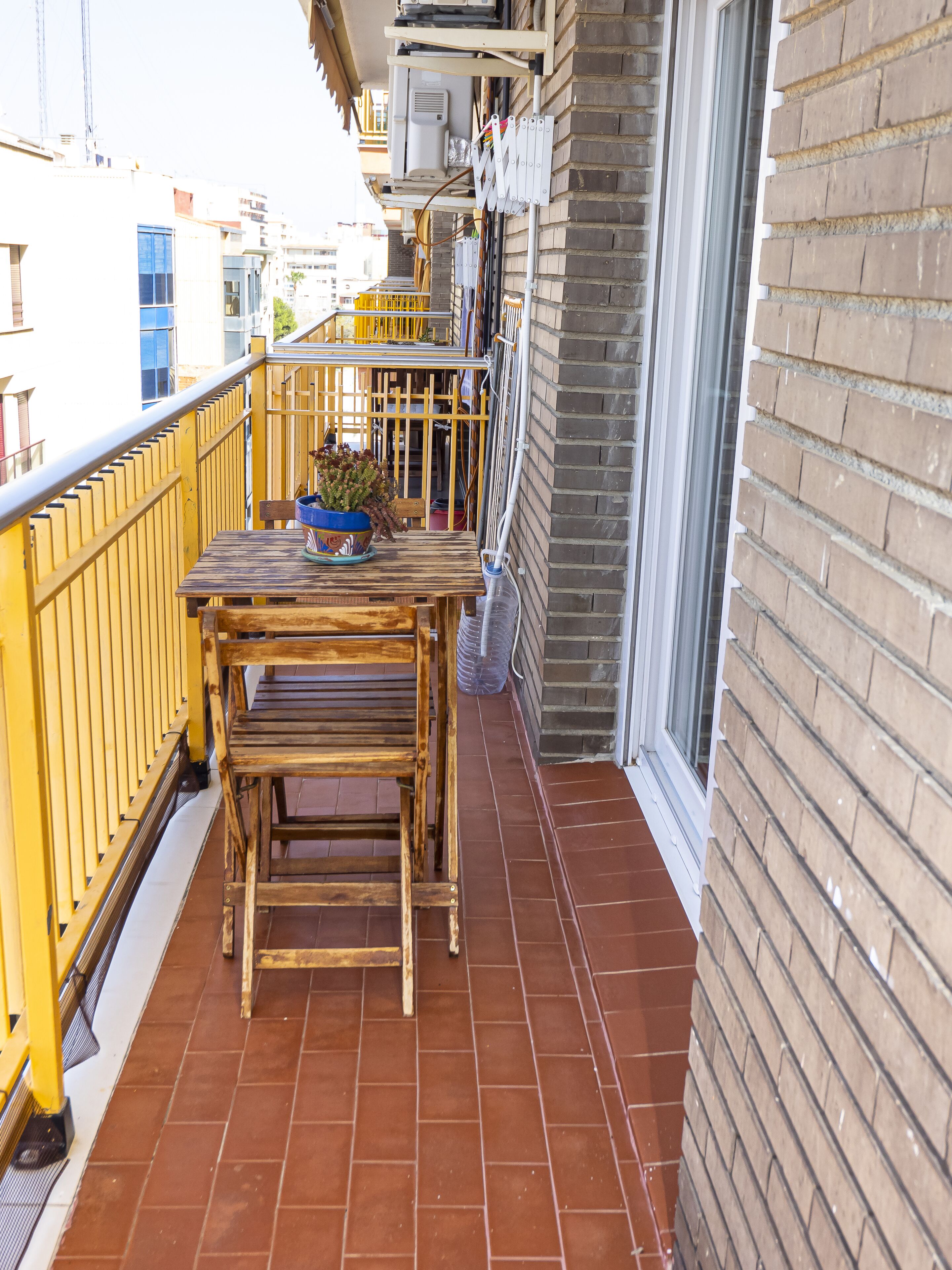 Un balcon avec une table et des chaises en bois, une plante en pot et une rambarde jaune.