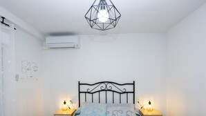 Ett sovrum med en säng, två sängbord, en hängande lampa, en luftkonditioneringsanläggning och en dörr.