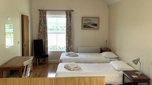 Une chambre d’hôtel avec deux lits, un bureau, une chaise, un radiateur et une fenêtre avec des rideaux.