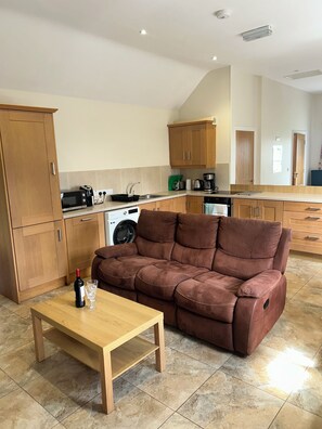 A modern kitchen with wooden cabinets, a sofa, a table, and a washing machine.