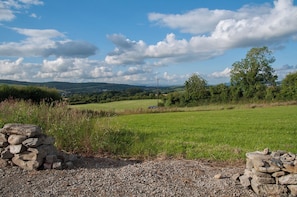 A rural landscape with a clear sky, rolling hills, and a stone wall in the foreground.