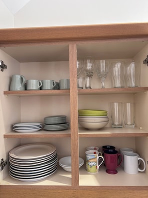 A kitchen cabinet with shelves holding plates, bowls, cups, and glasses.