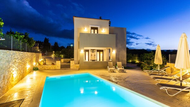 Uma casa moderna de dois andares com piscina, área de estar externa e muro de pedra.