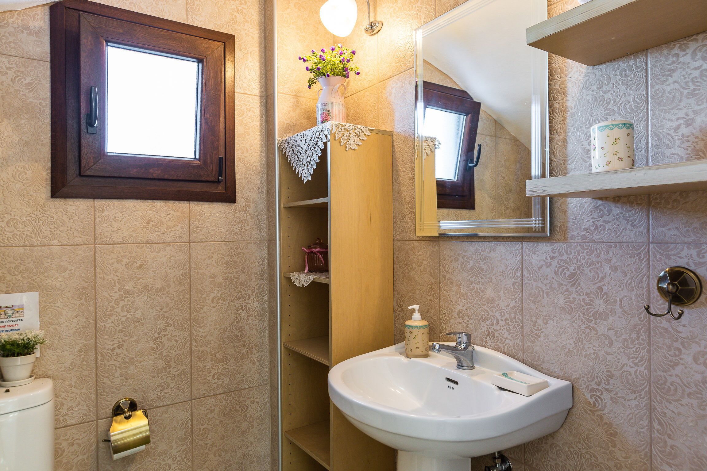 Ein Badezimmer mit einem Holzkosmetikschrank, einem weißen Waschbecken, einem Spiegel und einem Fenster mit Holzrahmen.