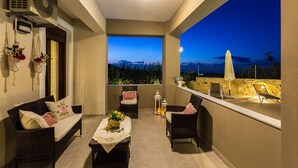 Uma varanda com móveis de vime, uma mesa com flores e vista para as montanhas ao entardecer.