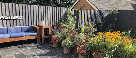 A patio area with a wooden bench, a small wooden table, and a sign reading "WHITTY LANE".