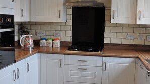 Cucina con mobili bianchi, piano cottura nero e piani di lavoro in legno.