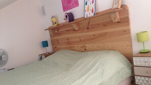Ein Schlafzimmer mit einem Holz-Kopfteil, einer grün gemusterten Bettdecke, einem Nachttisch mit Lampe und einem Wandregal mit Dekoration.