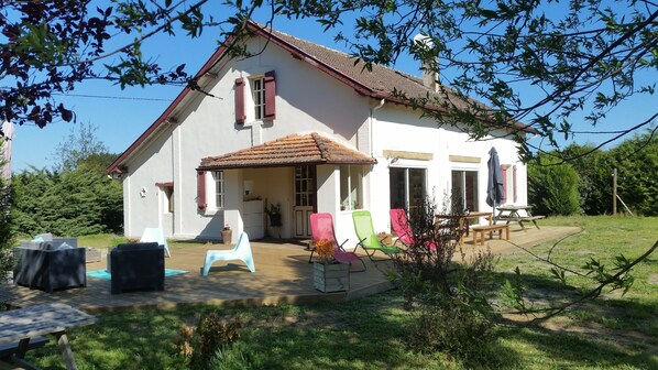 Una casa blanca con techo de tejas, un patio con mobiliario exterior y un jardín.