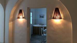 An arched hallway with two wall-mounted lamps, a dining area with a table and chairs, and a framed picture on the wall.