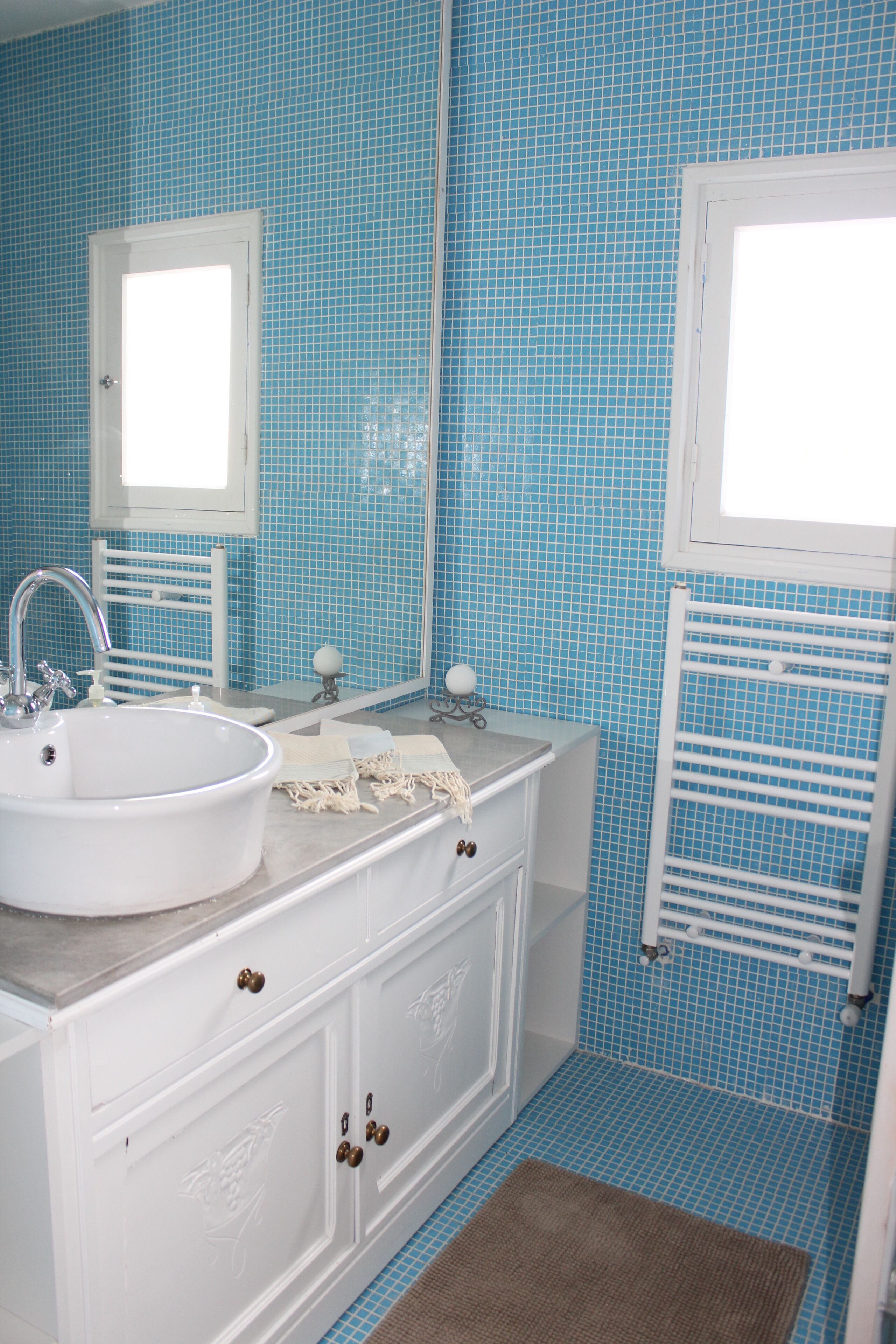 A bathroom with a white vanity, a sink, a mirror, and a window.