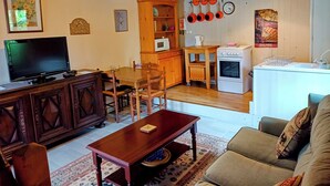 A cozy living room with a TV, wooden furniture, a dining area, and a kitchen with basic appliances. - LA GRANGE A CONVERTED BARN IN THE BEAUTIFUL HAMLET OF TALROCH (Melrand)