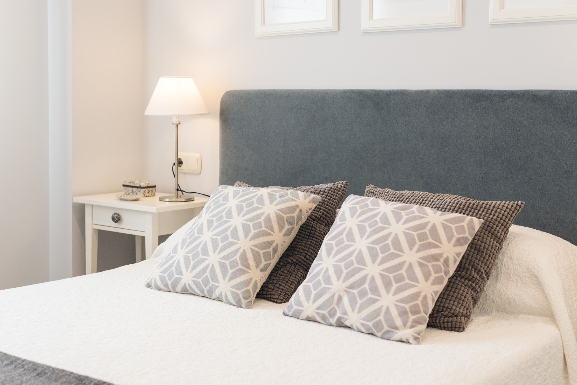 A neatly made bed with patterned pillows, a bedside lamp, and a small bedside table with a decorative item.