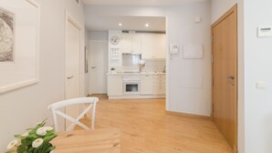 Ett modernt kök med vita skåp, en inbyggd ugn och en matplats med ett träbord och vita stolar.