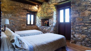 A room with two beds, stone walls, wooden beams, a fireplace, and a window with blinds. - Ruralmédulas Las Médulas - El Bierzo house 4 (Carucedo)