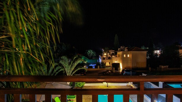 Ein Hotel mit Pool im modernen Stil, ein gut beleuchteter Balkon und umliegende Grünflächen bei Nacht.